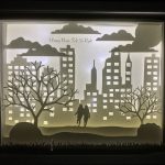 Artwork by Jessica Hotchkiss. Shadow box. two people in the middle of a city scene.